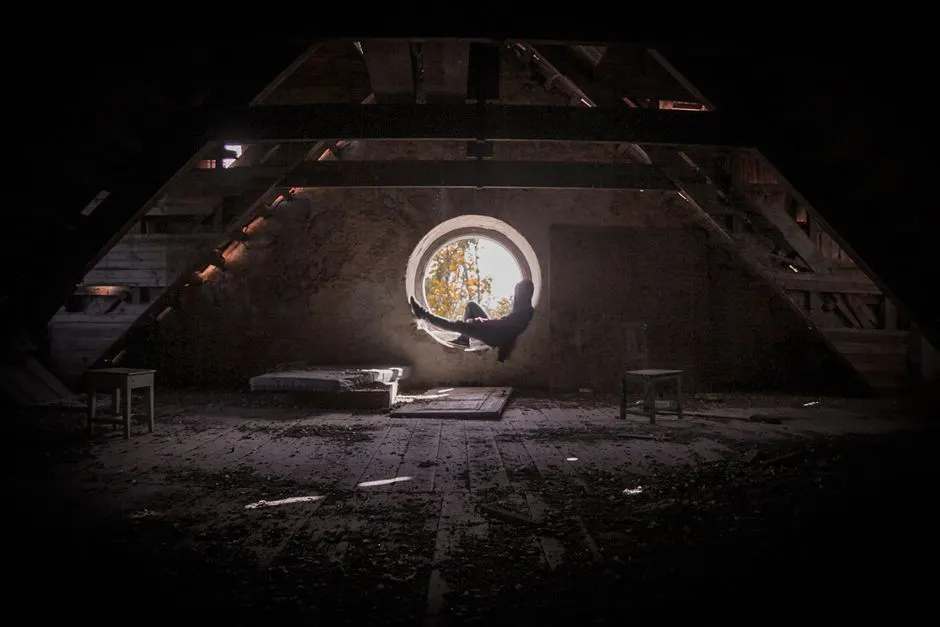 Atmospheric photo of a person sitting in an attic window, captured in warm autumn light.